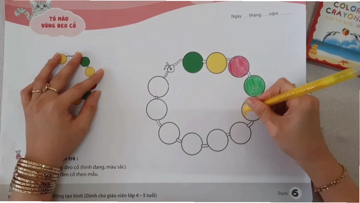 Cô giáo hướng dẫn bé cách cầm bút và tô màu vòng đeo cổ